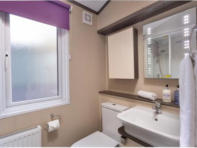 A bathroom with a toilet a sink a mirror a cabinet a window with a purple blind and toiletries at Lancashire Rose Ambleside