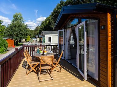 An outdoor patio with a wooden table and chairs set outside a cabin with glass doors open Lancashire Rose Ambleside
