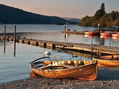 A wooden rowboat on a lakeshore near a wooden dock with red boats and a swan on the water at Lancashire Rose in Ambleside