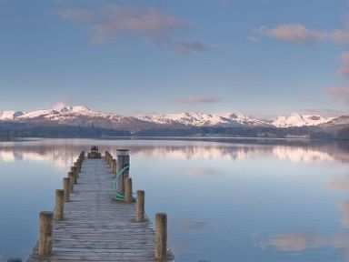 A wooden jetty extending into a calm lake with snow-covered mountains in the background at Lancashire Rose in Ambleside