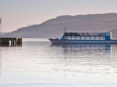 A boat on calm water near a pier with a hillside in the background at Lancashire Rose in Ambleside
