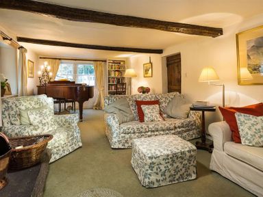 A living room with floral patterned sofas a piano a bookshelf and lamps at High Cleabarrow in Windermere