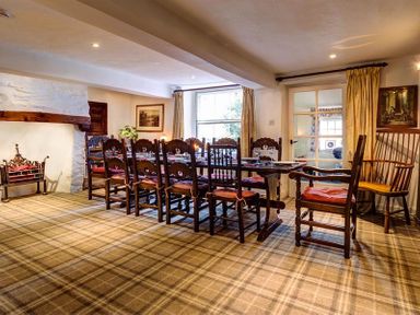 A dining room with a long wooden table and chairs near a window and fireplace at High Cleabarrow in Windermere