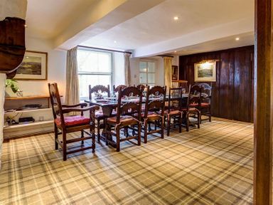 A dining room with a large wooden table surrounded by chairs and a window with curtains at High Cleabarrow in Windermere