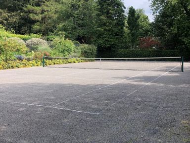 An outdoor tennis court surrounded by trees and bushes at High Cleabarrow in Windermere