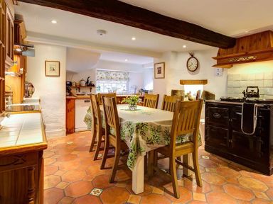 A kitchen with a dining table and six wooden chairs a stove and wooden cabinets at High Cleabarrow in Windermere