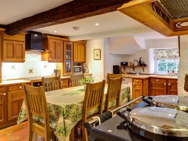A kitchen with wooden cabinets a dining table with chairs and a window at High Cleabarrow in Windermere