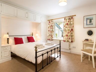 A bedroom with a double bed with red pillows two bedside lamps floral curtains and a small desk at High Cleabarrow in Windermere