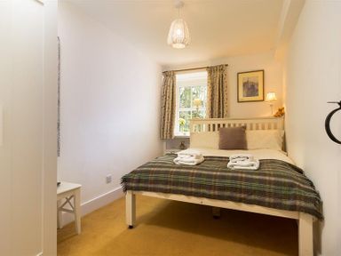 A bedroom with a double bed with folded towels a window with curtains and a bedside table with a lamp at High Cleabarrow in Windermere