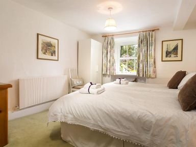 A bedroom with two single beds a window with patterned curtains a white wardrobe and framed pictures on the walls at High Cleabarrow in Windermere