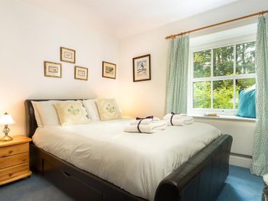 A bedroom with a bed and bedside table near a window with curtains at High Cleabarrow in Windermere