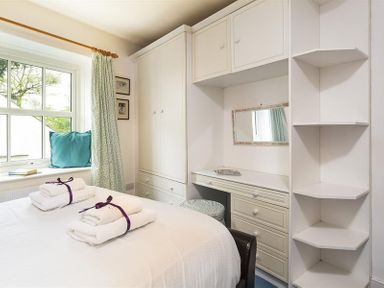 A bedroom with white cabinetry a window with patterned curtains and folded towels on a bed at High Cleabarrow in Windermere