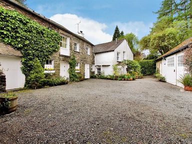 A courtyard with stone and white buildings surrounded by plants and trees at High Cleabarrow in Windermere