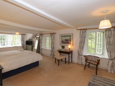 A bedroom with a bed a wooden desk with a chair a mirror a television and windows with curtains at High Cleabarrow in Windermere