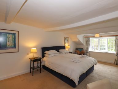 A bedroom with a double bed table lamps paintings an armchair and a window with curtains at High Cleabarrow in Windermere