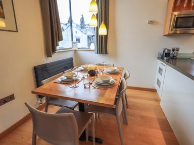 A dining area with a wooden table set with plates and glasses next to a window and kitchen at Idle Mill 2 in Ambleside
