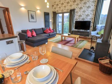 A living room and dining area with a gray sofa red pillows a wooden coffee table and a dining table set for four at Idle Mill 2 Ambleside