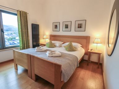 A bedroom with a wooden double bed two bedside tables with lamps a window with green curtains and three framed pictures at Idle Mill 2 Ambleside