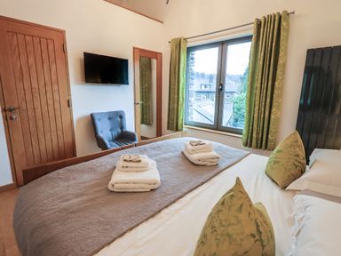 A bedroom with a bed with folded towels on it a grey chair a wall-mounted television and green curtains at Idle Mill 2 in Ambleside