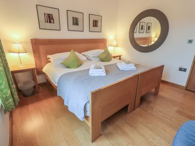 A bedroom with a double bed green pillows bedside tables with lamps and a round wall mirror at Idle Mill 2 in Ambleside