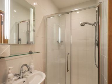 A bathroom with a sink faucet mirror glass shelf soap dispensers toilet paper and a shower with glass doors at Idle Mill 2 Ambleside