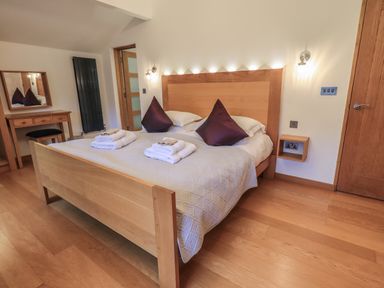 A bedroom with a wooden double bed with two pillows folded towels bedside lights a dressing table with mirror and chair at Idle Mill 2 Ambleside