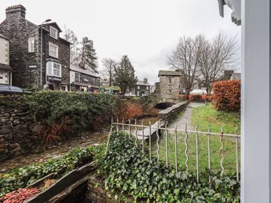 A small stone bridge over a stream with stone buildings and people walking nearby in a village setting at Idle Mill 2 in Ambleside