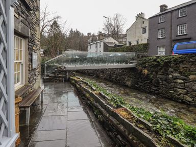 A wet stone pathway beside a narrow water channel with stone walls and a glass bridge above at Idle Mill 2 Ambleside