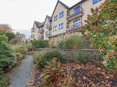 A gravel path leading to a three-story residential building with balconies and surrounding plants at Waterhead Retreat in Ambleside