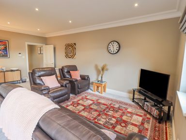 A living room with leather chairs a patterned rug a flat screen tv on a stand and a wall clock at Waterhead Retreat Ambleside
