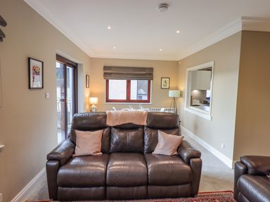 A living room with a dark leather sofa two cushions a window and a dining table at Waterhead Retreat in Ambleside