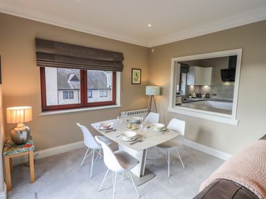 A dining area with a square table set for four and white chairs near a window and an open kitchen at Waterhead Retreat Ambleside