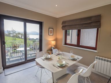 A dining room with a set table and sliding glass door opening to a balcony with a view at Waterhead Retreat in Ambleside