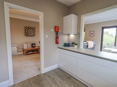 A kitchen area with white cabinets and a countertop looking into two adjoining rooms at Waterhead Retreat in Ambleside