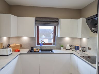 A kitchen with white cabinets a window above the sink a toaster kettle bread box and stovetop at Waterhead Retreat in Ambleside