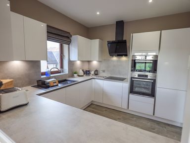 A kitchen with white cabinets a black stove and oven a toaster and a window at Waterhead Retreat in Ambleside