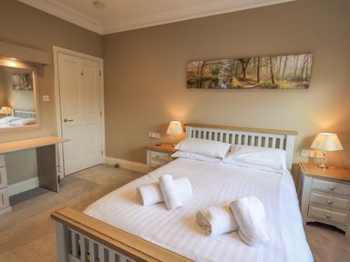 A bedroom with a double bed towels on the bed bedside tables with lamps a door and a dressing table with a mirror at Waterhead Retreat in Ambleside