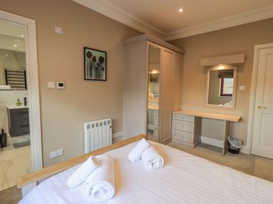 A bedroom with a bed with towels, wardrobe with mirrored doors, desk with drawers, wall mirror, and an adjacent bathroom at Waterhead Retreat in Ambleside