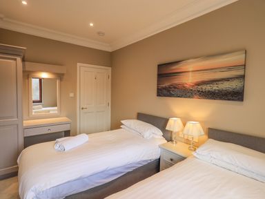 A bedroom with two single beds bedside table with two lamps wardrobe and a framed mirror on the wall at Waterhead Retreat in Ambleside