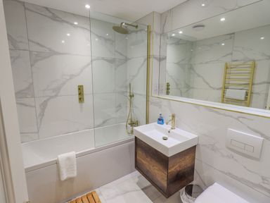 A bathroom with a bathtub shower combination a sink with wooden cabinet and a large mirror at Waterhead Retreat in Ambleside