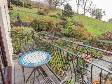 A balcony with a round table and two chairs overlooking a garden and hillside at Waterhead Retreat Ambleside