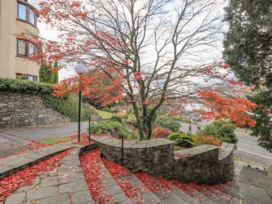 A stone staircase with red leaves on the steps and a tree with red leaves next to a road at Waterhead Retreat in Ambleside