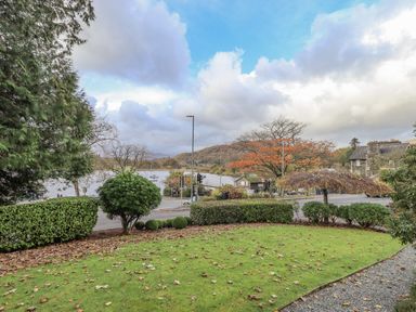 A garden with green grass and bushes overlooking a road a lake and hills at Waterhead Retreat in Ambleside