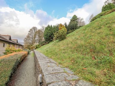 A gravel path with a stone wall and grass slope alongside a building at Waterhead Retreat in Ambleside