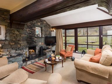 A living room with stone wall fireplace sofas armchair coffee table and large windows at Thirlmere Cottage in Grasmere