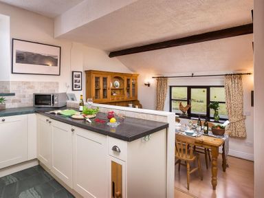 A kitchen with a countertop and a dining area with a wooden table and chairs at Thirlmere Cottage in Grasmere