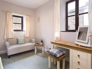 A small room with a sofa a side table with a teapot and cup a dressing table with mirror stool and lamp at Thirlmere Cottage in Grasmere