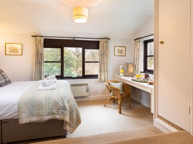 A bedroom with a bed and a desk with a chair beside windows at Thirlmere Cottage in Grasmere