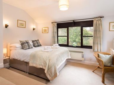 A bedroom with a bed two plaid pillows a wicker chair and a window with curtains at Thirlmere Cottage in Grasmere