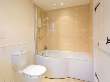 A bathroom with a toilet and a bathtub with showerhead and glass screen at Thirlmere Cottage in Grasmere